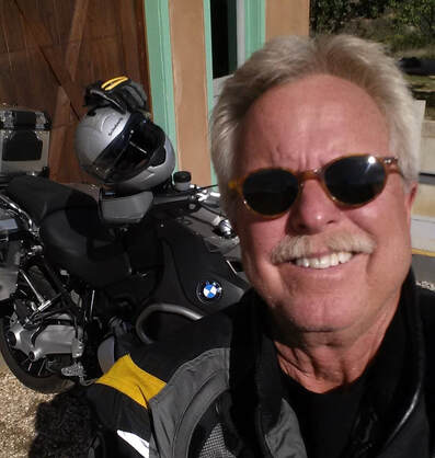 Gary, the director of Banditas WIld Horse Promise, smiling in the sun and some shades in front of his motorcycle.